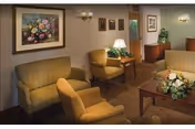 A comfortable senior living lounge with sofas, chairs, coffee table, wall art, and lamps.
