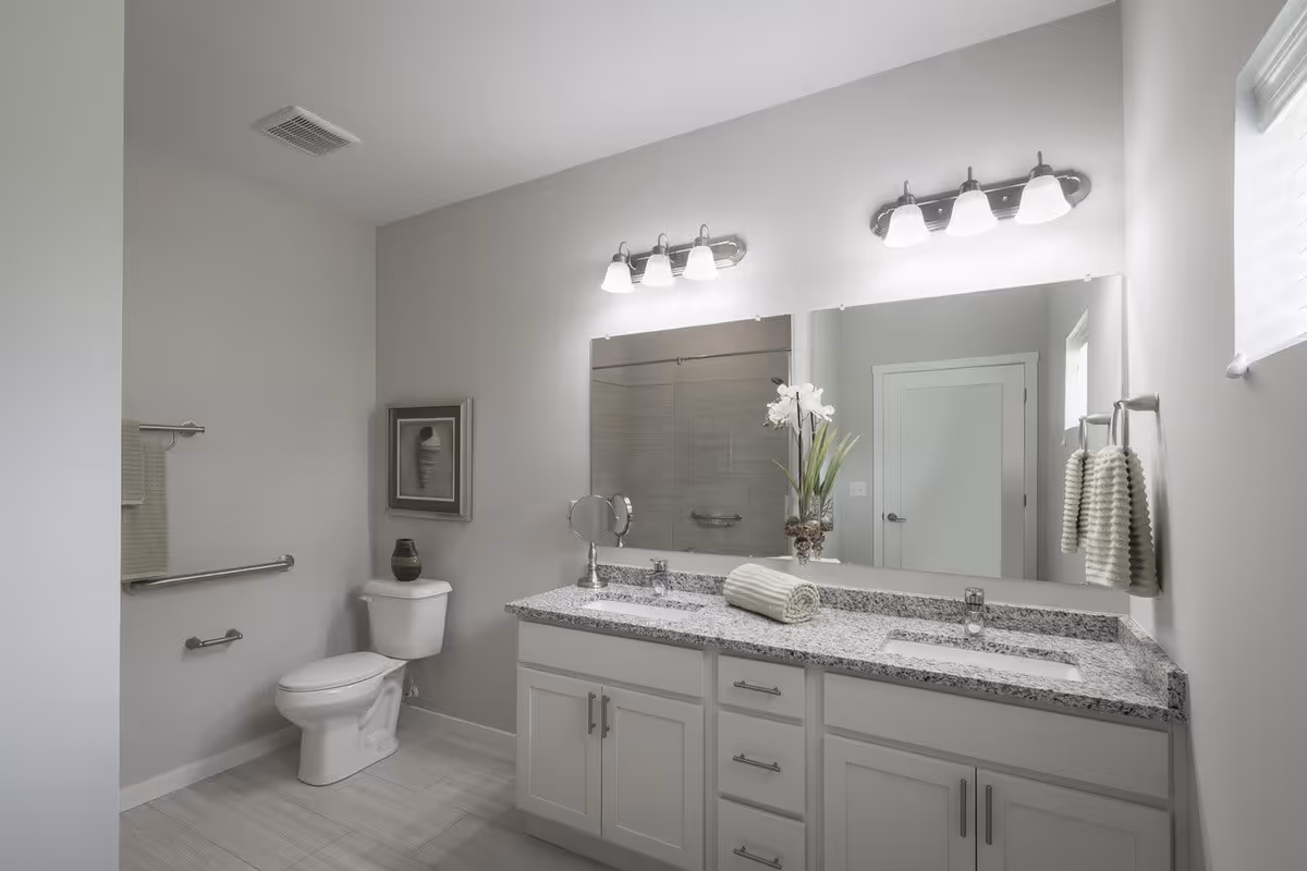 Bright modern bathroom with a double-sink granite vanity, large mirror, toilet, and towel bars.