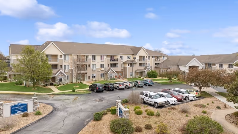 Front exterior of the College View Manor senior living building with a parking lot, landscaped beds, and parked cars.