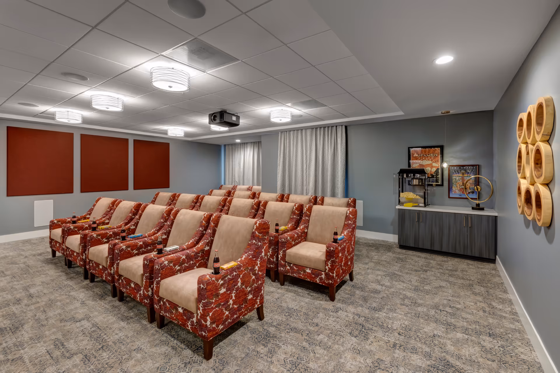 Small screening room with rows of patterned armchairs facing a ceiling-mounted projector and a snack counter.
