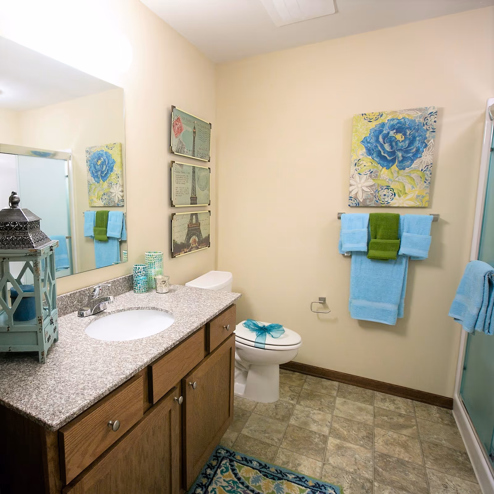 Bright bathroom with a granite countertop vanity, sink, toilet, shower, decorative towels and wall art.