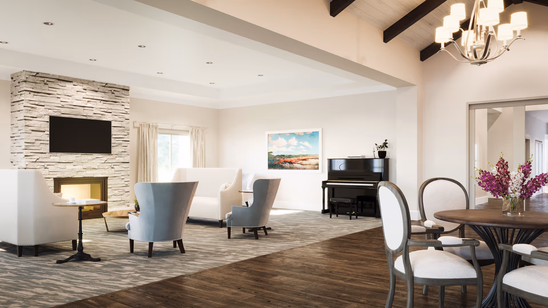 Bright furnished common living area with sofas and armchairs around a stone fireplace and TV, a piano against the wall, and a dining table with chairs and flowers.