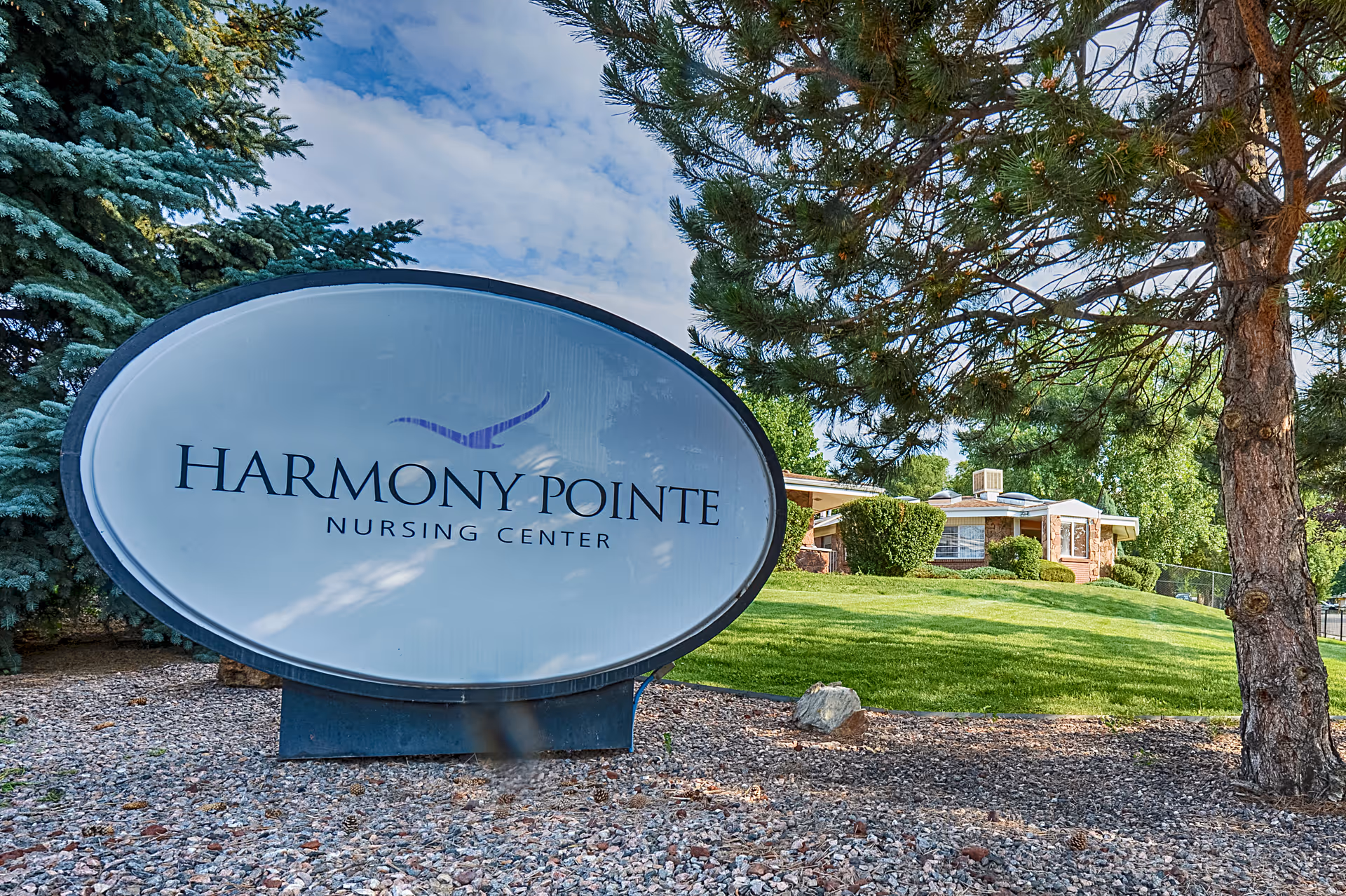 Oval sign reading "Harmony Pointe Nursing Center" on landscaped grounds in front of the facility building.