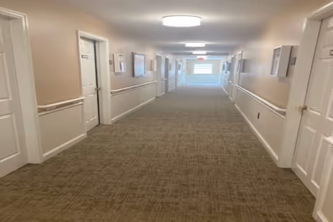 Carpeted interior hallway with doors and handrails on both sides leading to a windowed end.
