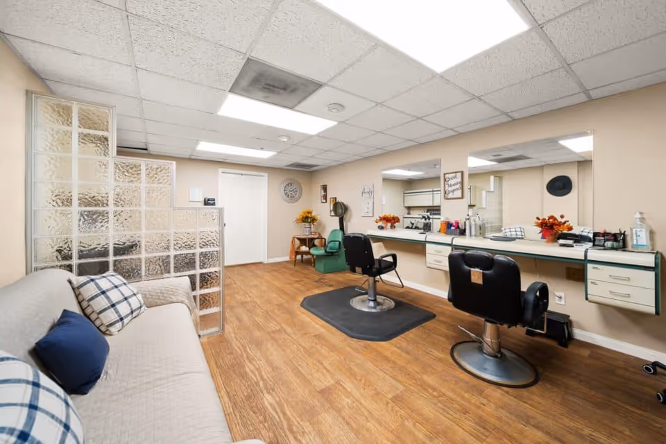 Interior salon/barber area with two styling chairs in front of mirrors, a couch, and a glass block partition.