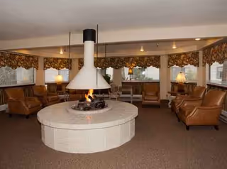 Round fireplace centerpiece surrounded by brown leather lounge chairs in a cozy common room.