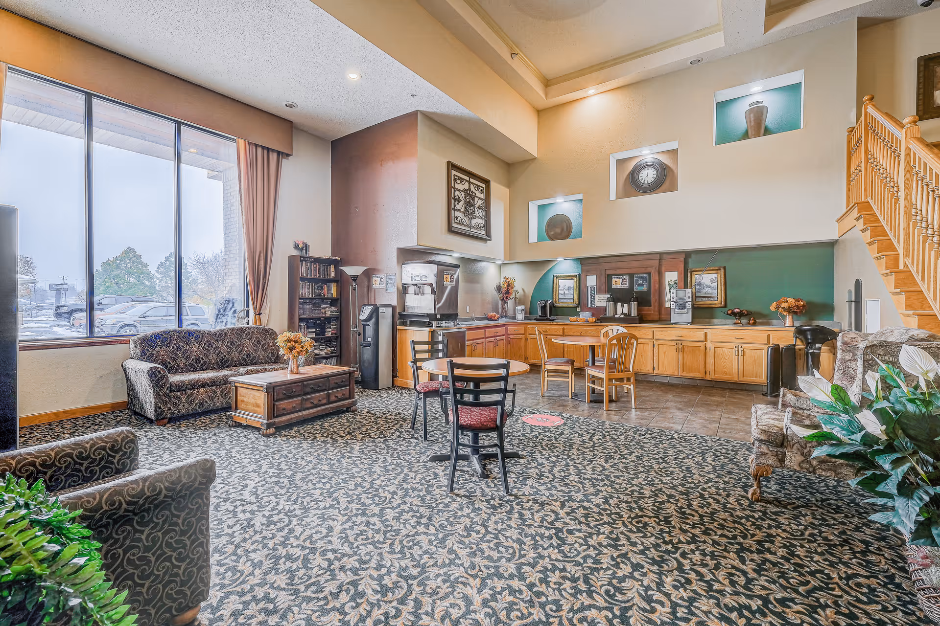 Bright communal lounge with sofas, chairs, a coffee station, large window and a staircase.