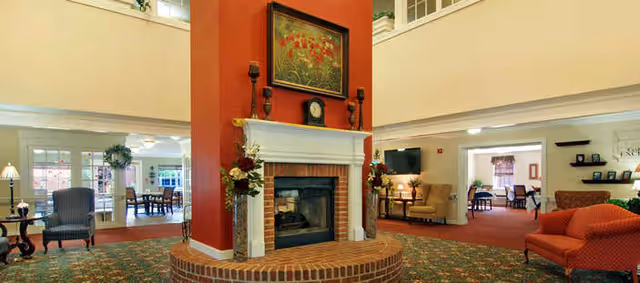 Interior common area with a central brick and white-mantled double-sided fireplace, seating, and patterned carpet.