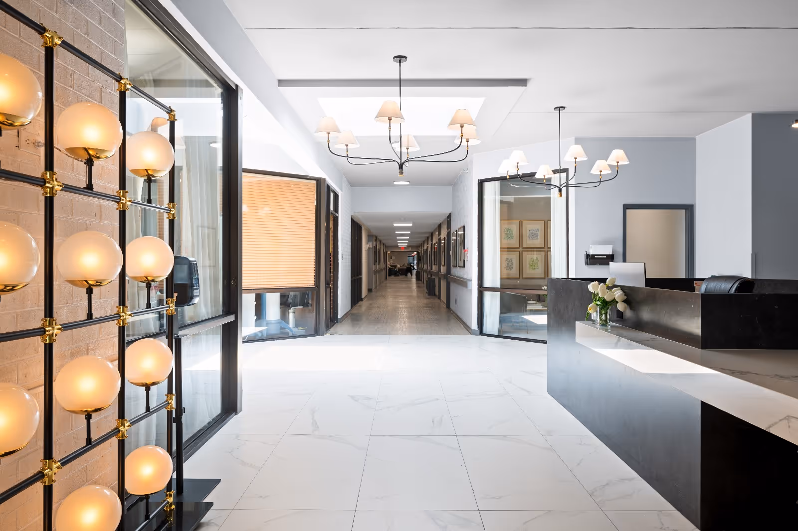 Bright modern reception lobby with a front desk on the right, decorative globe lamps on the left, and a long corridor ahead.