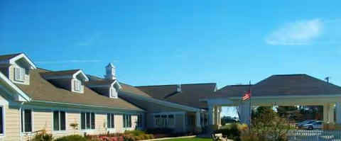 Long single-story senior living building with a covered entrance and American flag under blue sky.