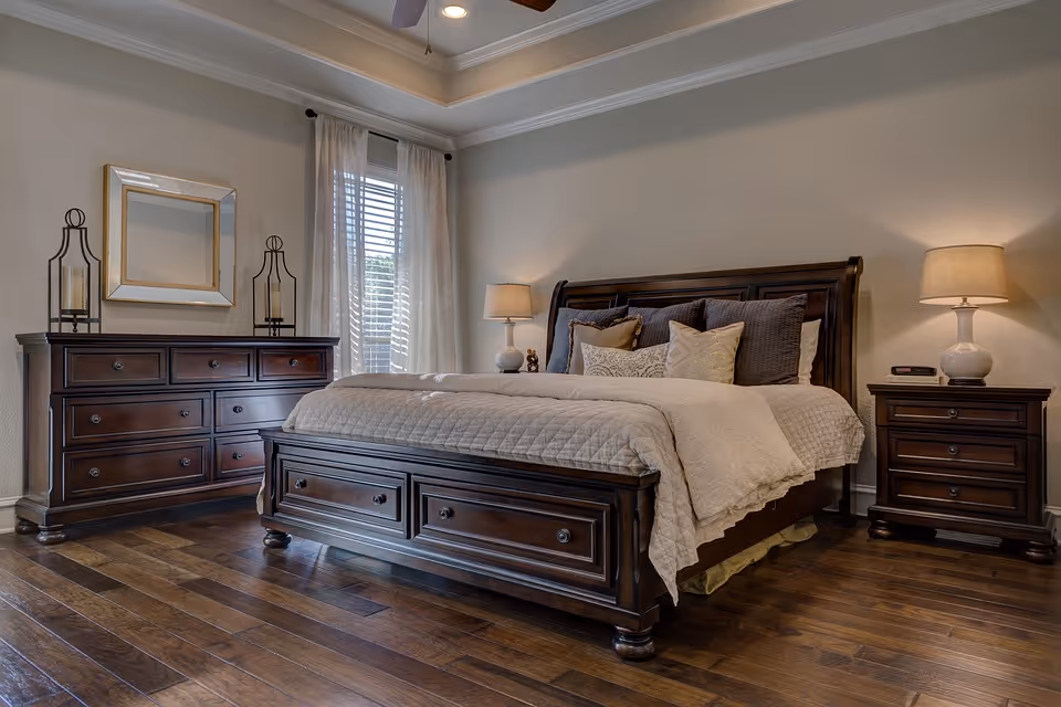 Well-appointed bedroom with a dark wood bed, matching dressers, bedside lamps, and hardwood floors.