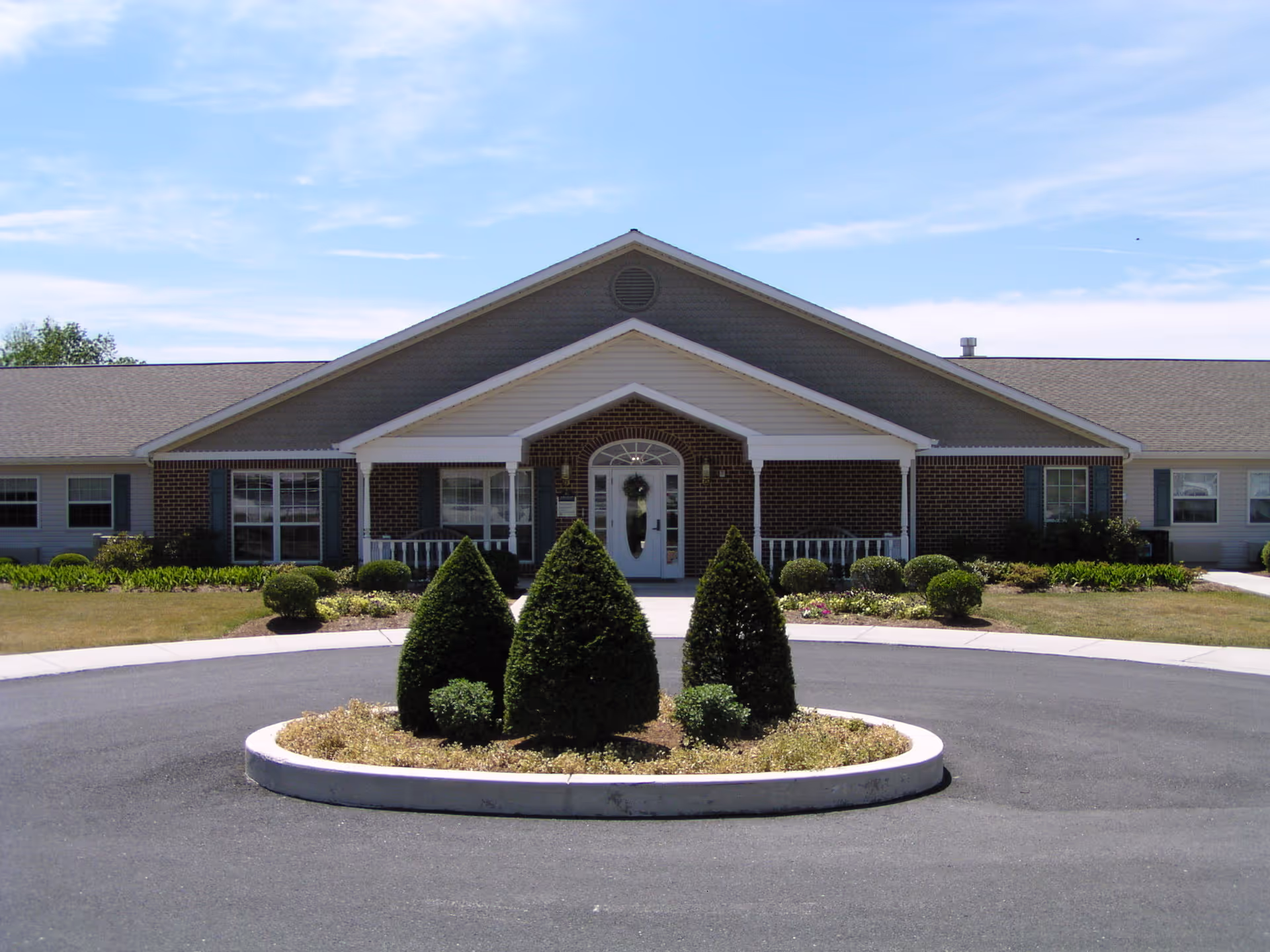 Front view of a single-story brick senior care building with a circular driveway and manicured shrubs.