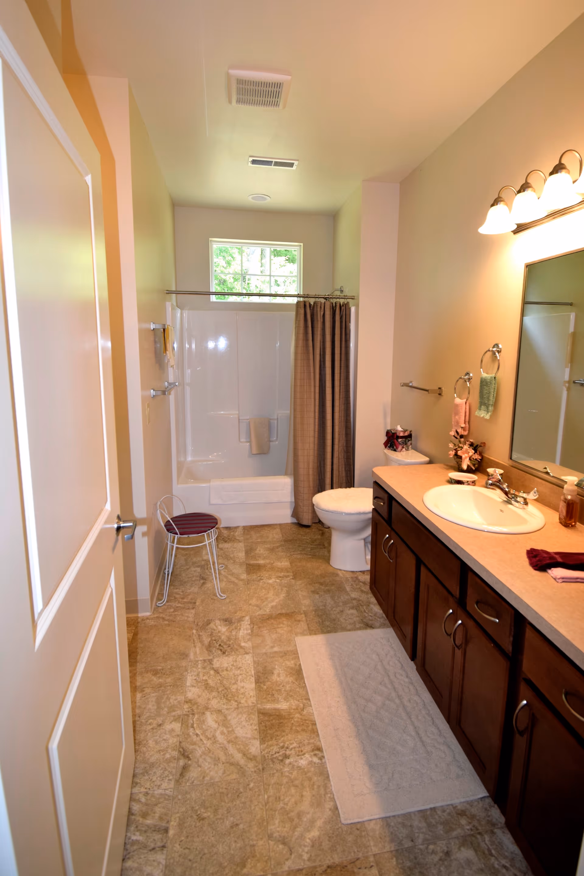 Bathroom with a sink and vanity on the right, a toilet and a shower-tub with curtain at the back, and a tiled floor.