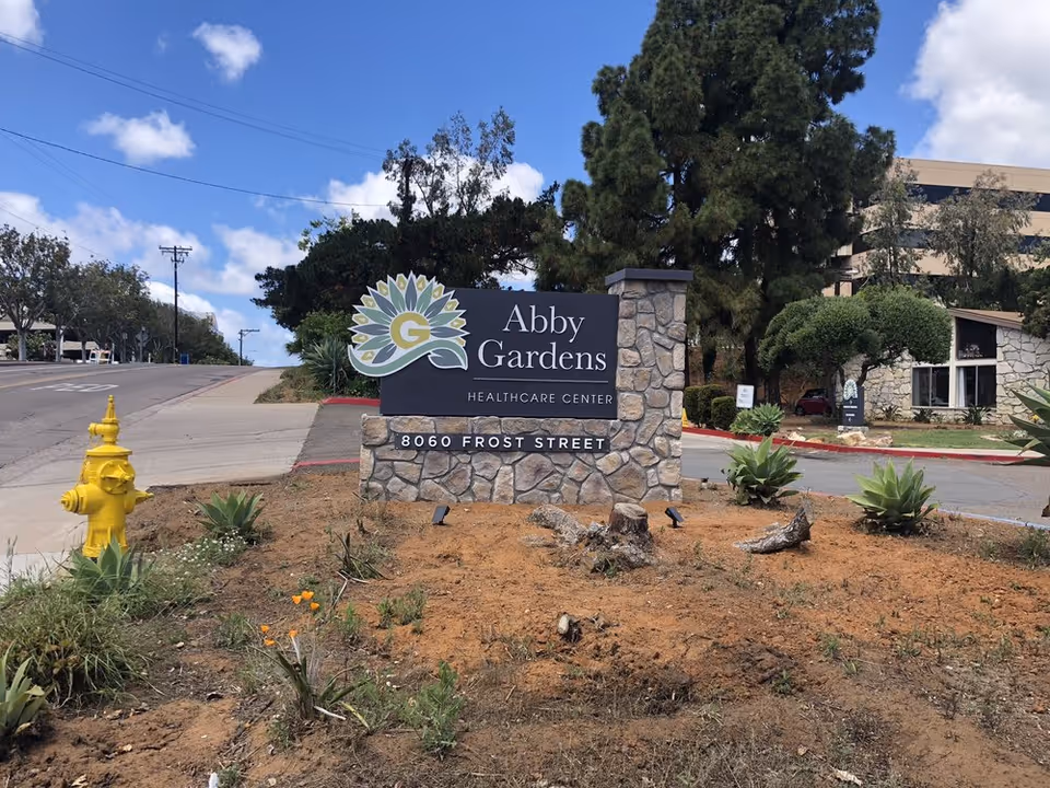 Stone sign for Abby Gardens Healthcare Center with surrounding landscaping by the street.