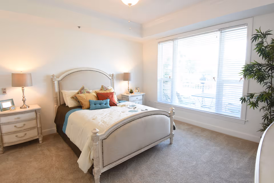 Bright furnished bedroom with a decorative bed, two nightstands and a large window with blinds.