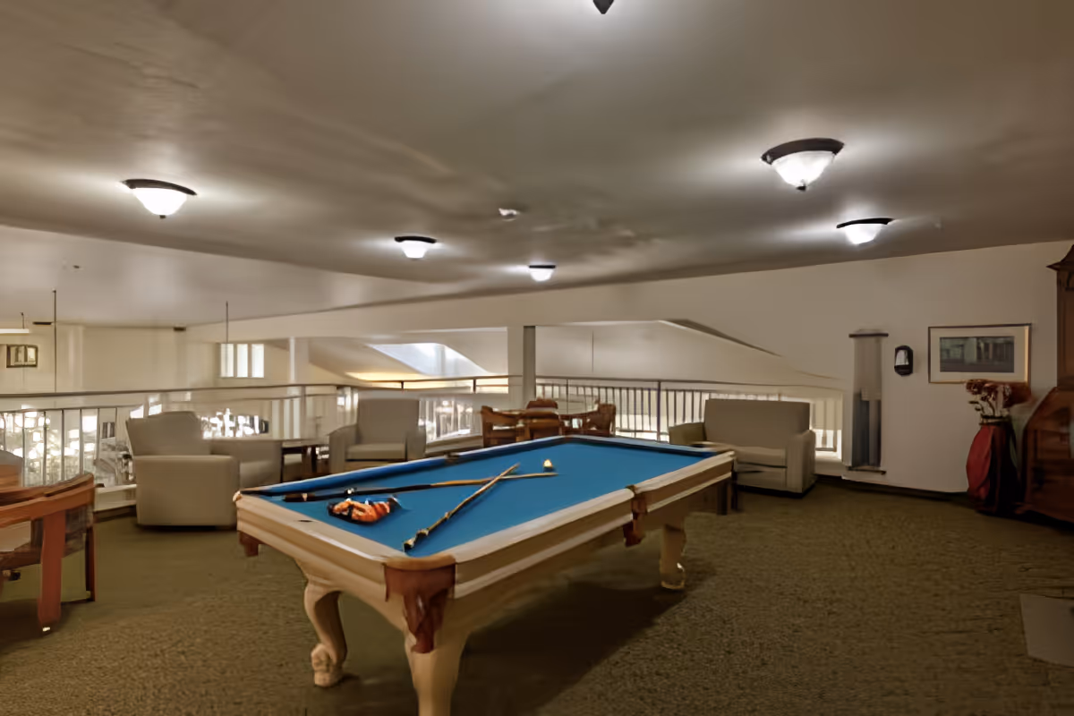 Indoor common lounge area with a blue pool table, seating and overhead lights.