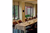 A dining room with a long table set with place settings and chairs alongside large windows overlooking greenery.
