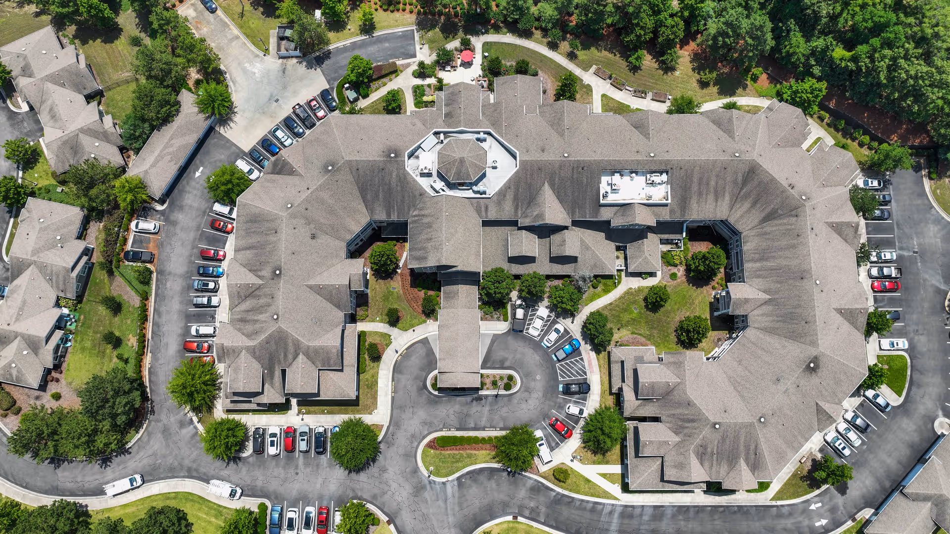 Aerial view of Southern Pines Gracious Retirement Living facility showing a large, multi-wing building with a central entrance driveway, surrounded by parking lots, landscaped green areas, and smaller adjacent buildings.