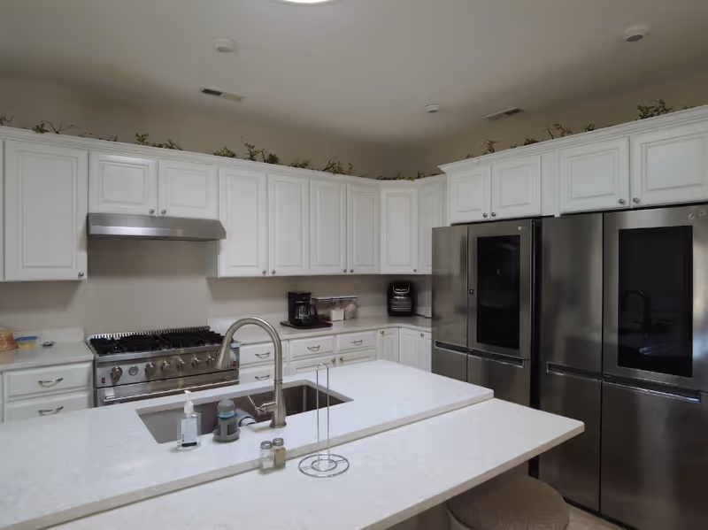 Spacious kitchen featuring white cabinetry, a large center island with sink, a gas range with hood, and stainless steel refrigerators.