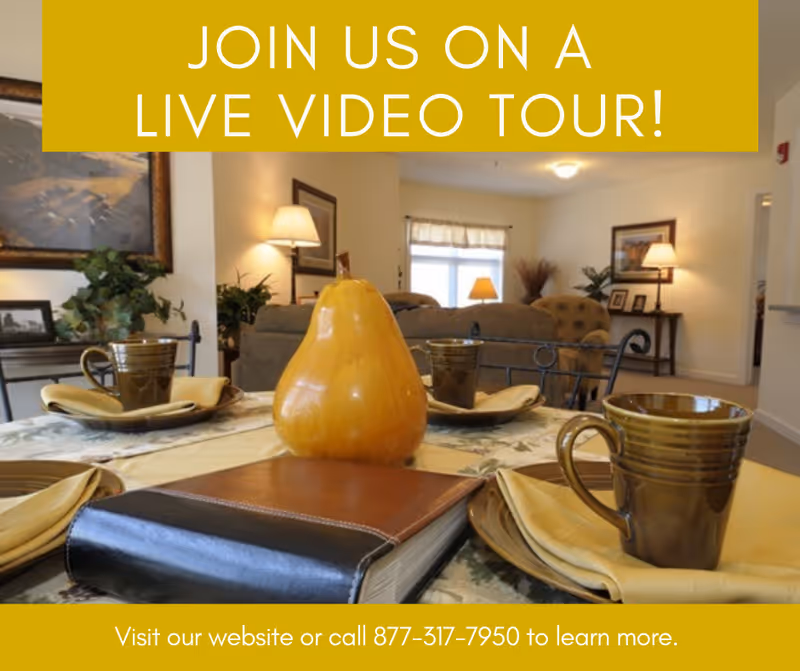 A dining table set with brown ceramic mugs, yellow napkins, and a decorative yellow pear centerpiece in a cozy living room setting with lamps, framed pictures, and plants in the background.