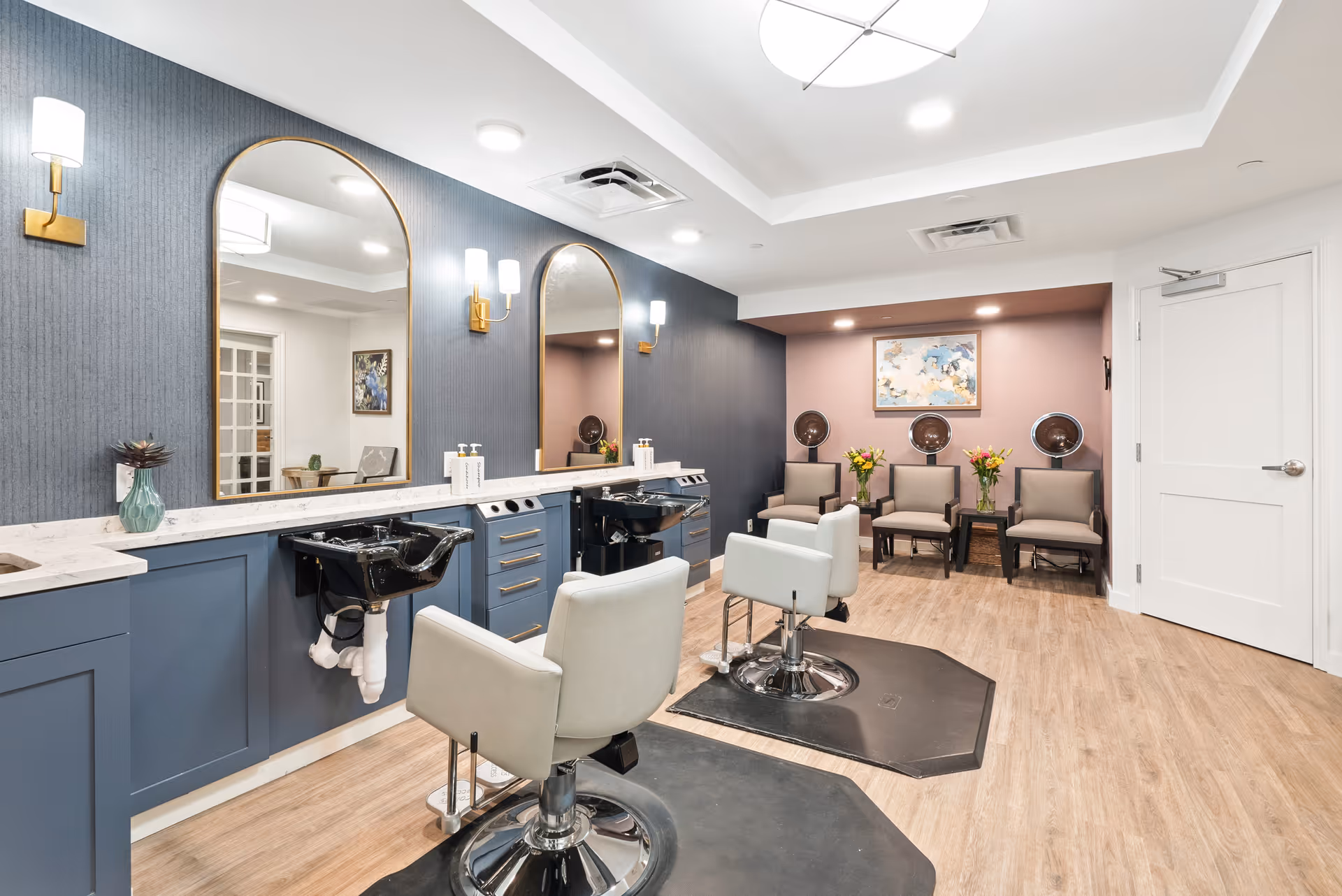 A bright salon area with styling chairs, shampoo sinks, arched mirrors, and a seating/waiting area.