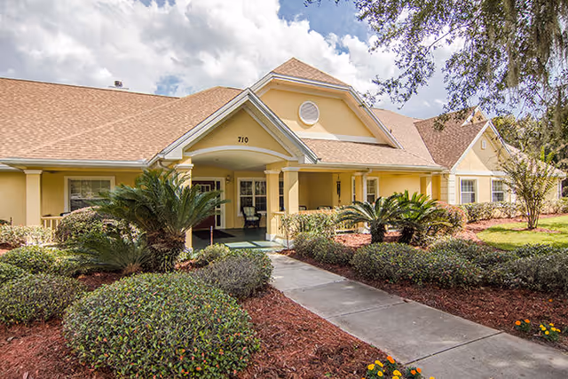 Front entrance of a yellow residential building with a covered porch, columns, and landscaped walkway.