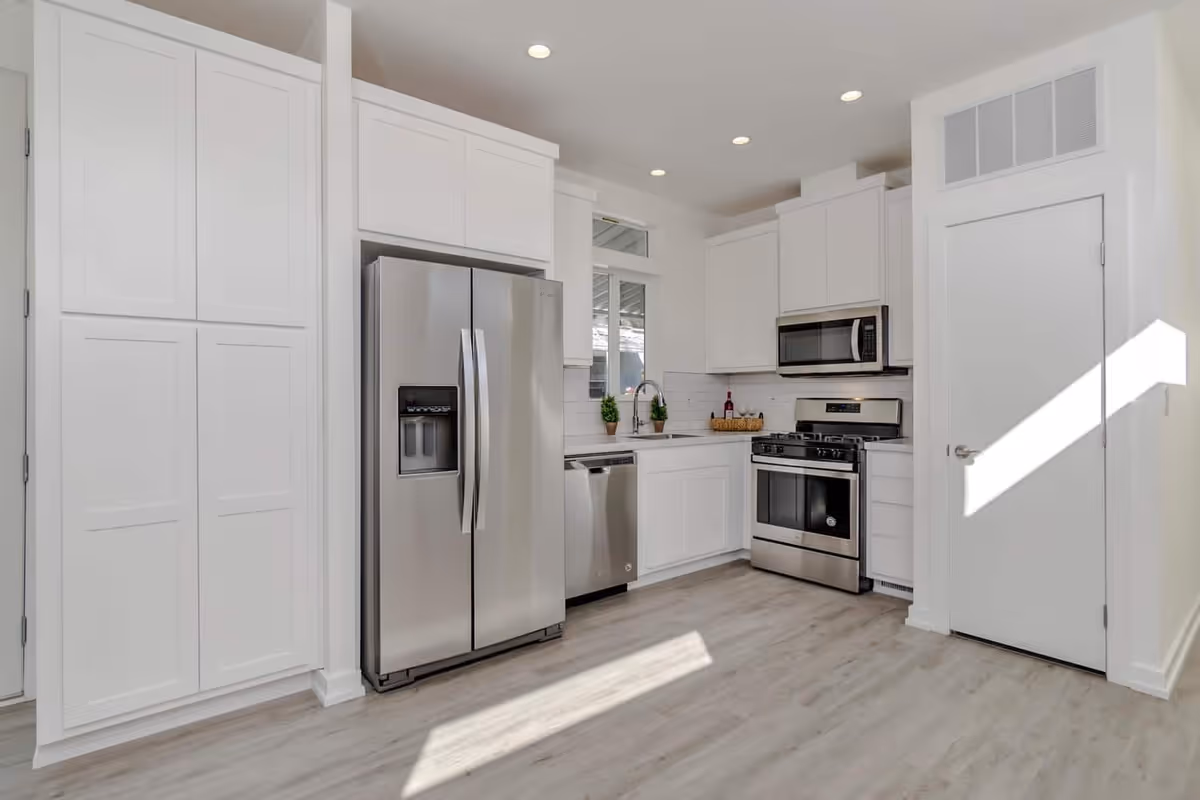 Bright modern kitchen with white cabinets and stainless steel refrigerator, dishwasher, oven, and microwave.