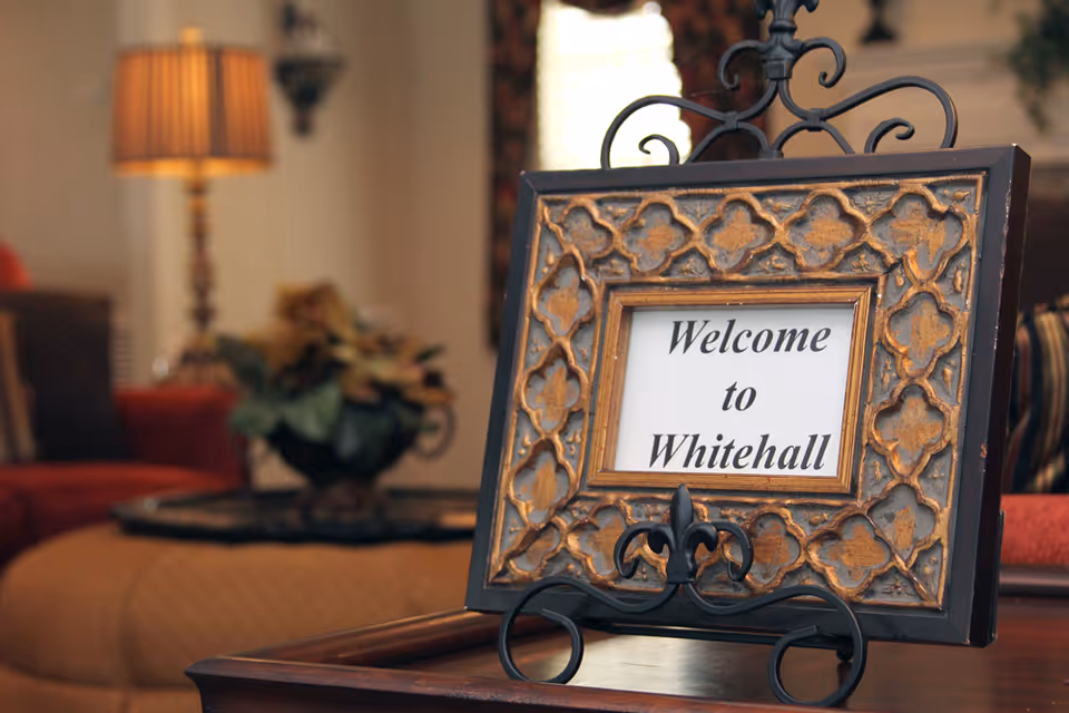 Ornate framed sign on a table reading "Welcome to Whitehall" in a cozy seating area.