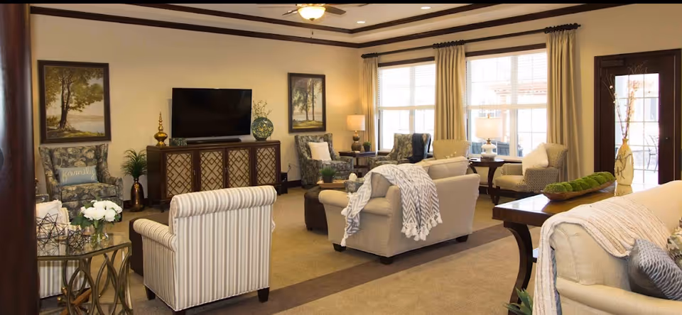 Well-lit communal living room with sofas, armchairs, a TV console and large windows.