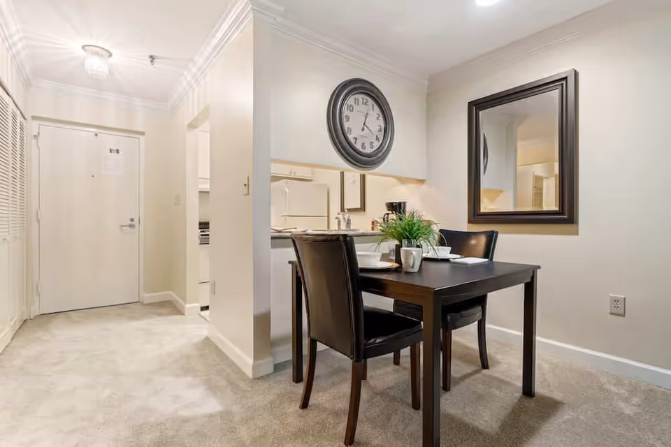 Small dining area with a dark table and two chairs beside a pass-through to the kitchen and the apartment entryway.