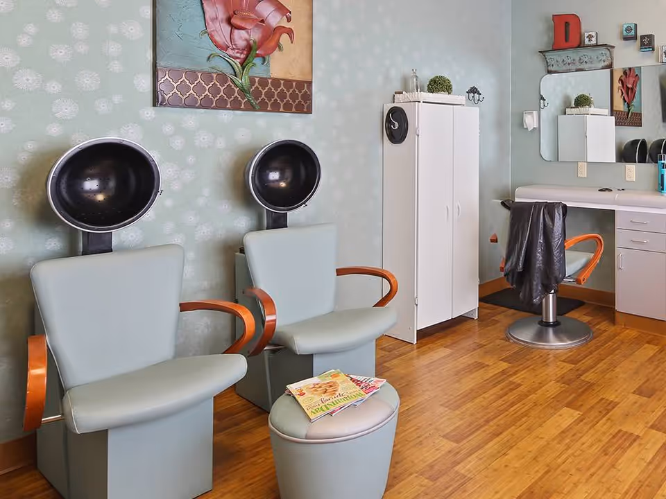 Interior salon room with two hooded hair dryers, salon chairs, a styling chair and cabinets.