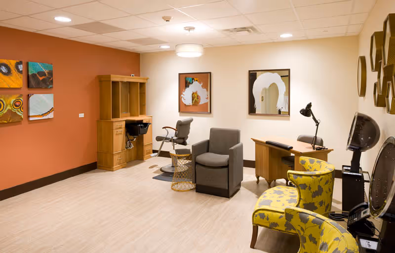 Bright interior common room with salon stations, armchairs, a desk and colorful wall art.