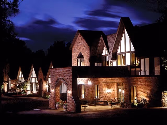 Brick Tudor-style residential building lit at night with an arched entrance and illuminated windows.