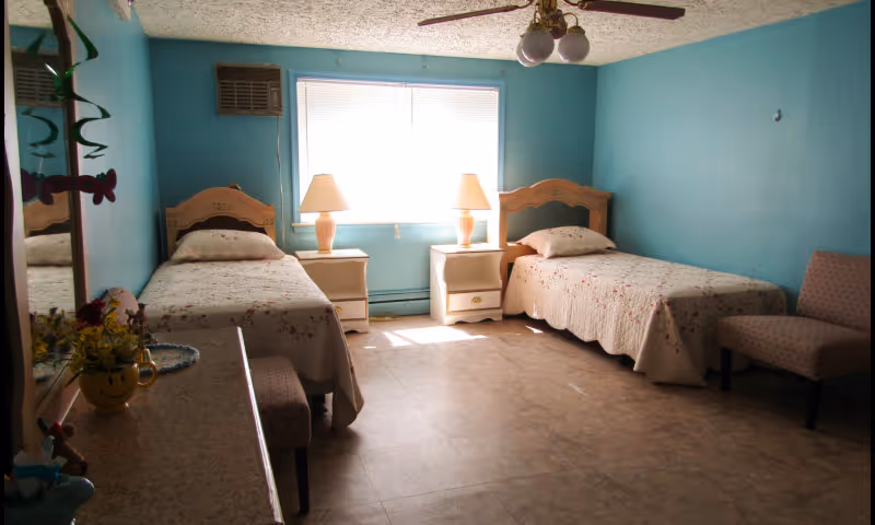 Small bedroom with two twin beds separated by nightstands and lamps under a central window and teal walls.