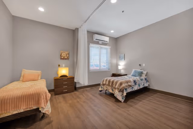 Shared bedroom with two single beds separated by a nightstand, a curtained room divider, window with blinds, and wood flooring.