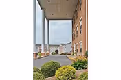 Covered entrance/porte-cochere of a brick nursing facility with white columns, driveway, and landscaped shrubs.