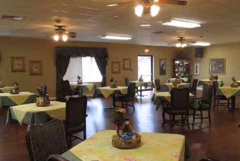 A senior living dining room with multiple tables, chairs, and pastel tablecloths.