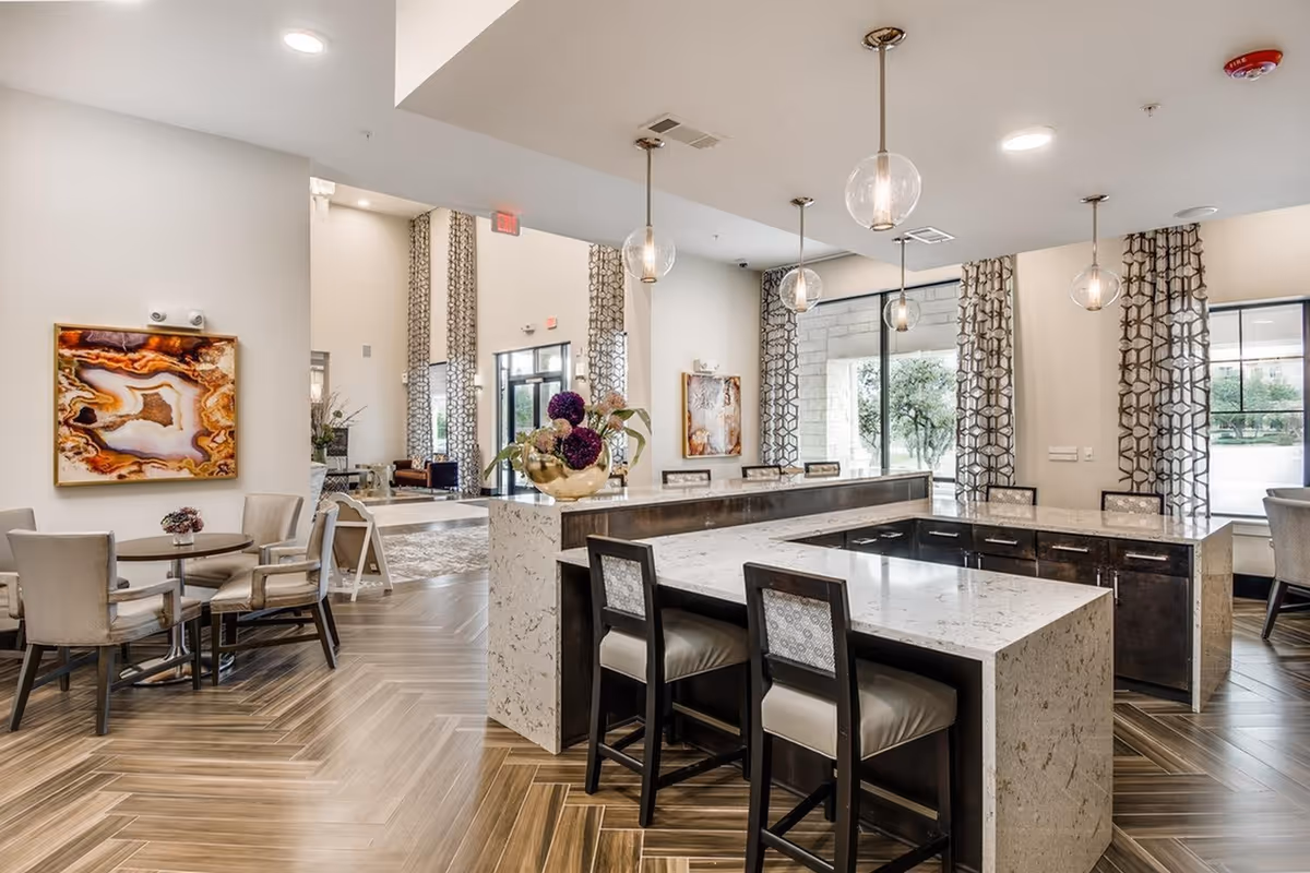 Bright modern communal lounge and kitchen area with a large marble island, bar stools, pendant lights, and seating tables.