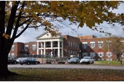 Brick senior living facility with a columned front entrance, parked cars, and autumn trees.