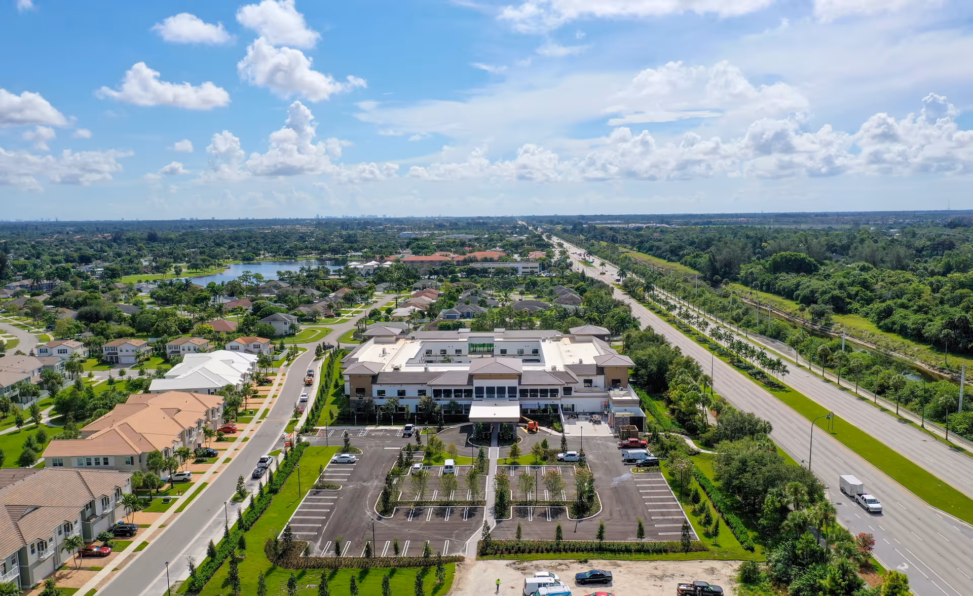 Aerial view of Bella Mar Royal Palm Beach facility surrounded by residential houses, greenery, and roads under a partly cloudy sky.