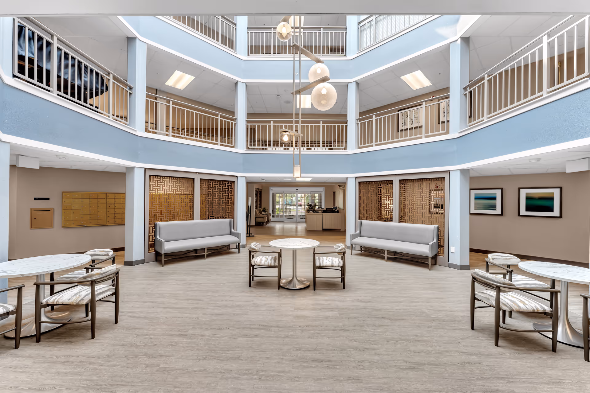 Bright multi-level atrium lobby with seating, round tables, and balconies in a senior living facility.