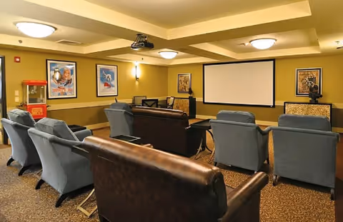 A cozy media room with rows of armchairs and leather sofas facing a projector screen and movie posters on the walls.