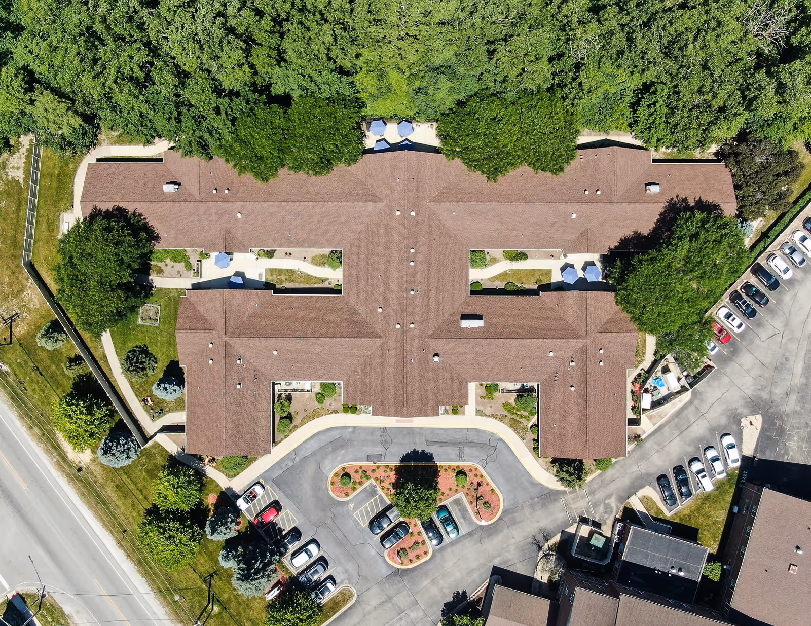 Aerial view of Arden Courts - ProMedica Memory Care Community in Palos Heights showing the building with a brown roof surrounded by trees, parking lots with cars, and landscaped areas.