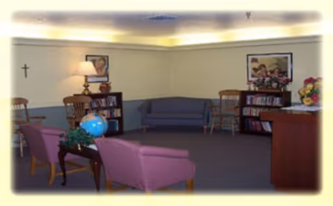 A common sitting room with armchairs, a sofa, bookshelves, lamps and framed artwork on the walls.