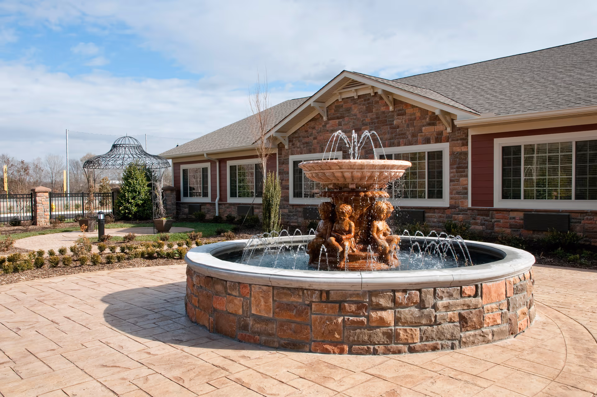 A decorative stone fountain in a paved courtyard in front of a single-story brick building.