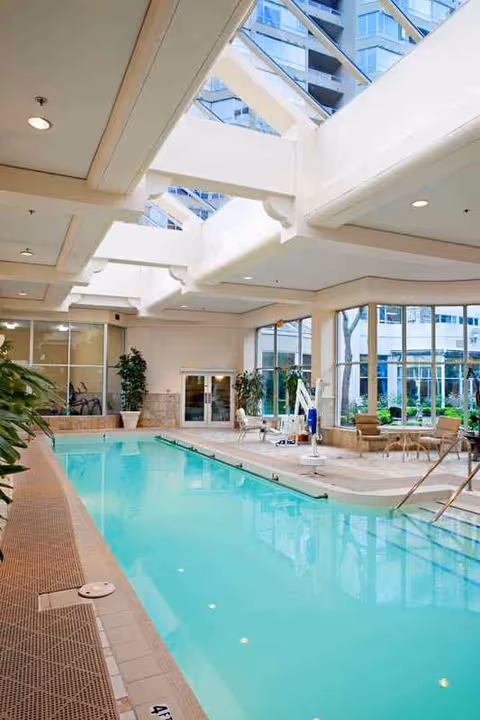 Indoor pool area with lounge seating, glass walls, and potted plants.