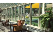 Sunlit glass-enclosed seating area with wicker chairs, cushioned sofa, and small table.