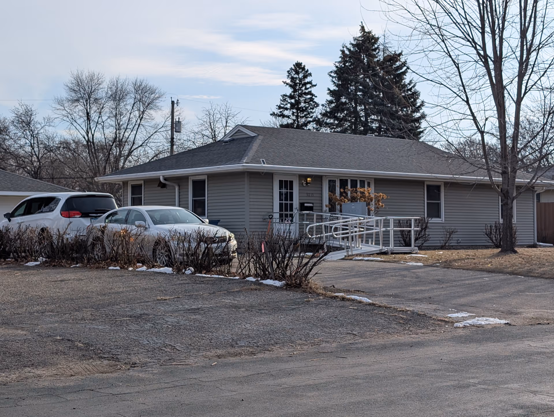 Single-story ranch-style building with a front wheelchair ramp, parked cars, and bare winter trees.