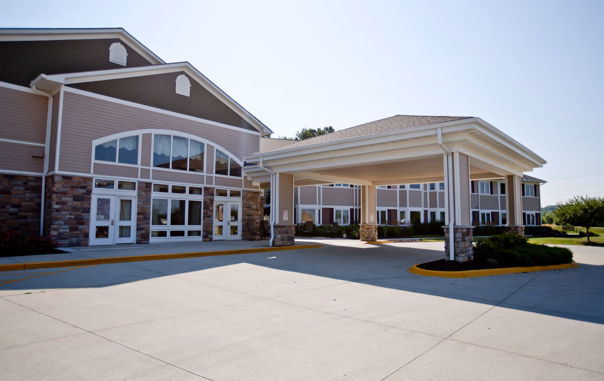 Front entrance of a multi-story assisted living building with a covered porte-cochere and large windows.
