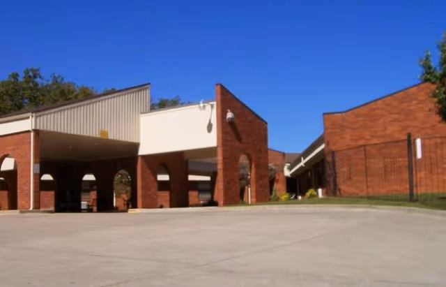 Exterior view of a brick building with a covered entrance and a clear blue sky above, showing part of the Warsaw Health and Rehabilitation Center.